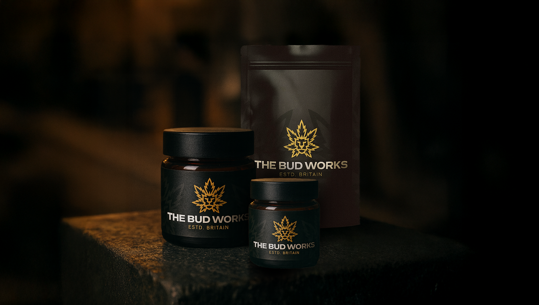 two black jars and one black mylar bag with the bud works branding situated on a block with low lighting and moody.