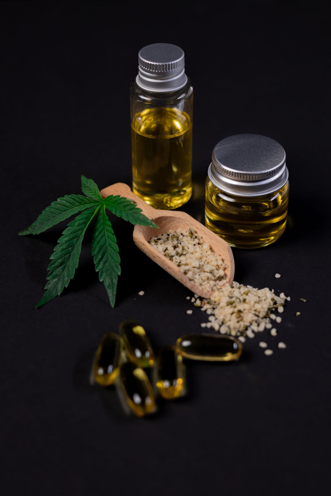 Hemp leaf, hemp seeds and hemp oil in glass jars on a dark background, alongside softgel capsules