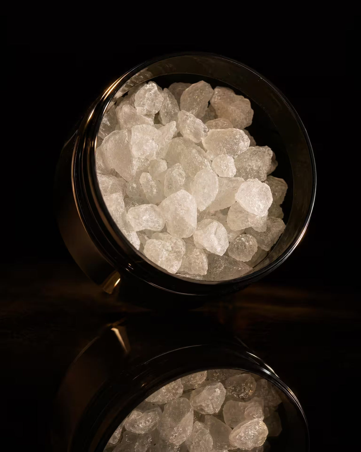 close up of thca diamonds in a black jar on a reflective surface.